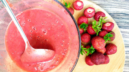 Whole strawberries lie on a cutting board. Glass cup with fruit and berry puree. Harvesting useful food for future use. View from above.の写真素材