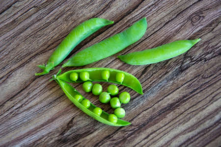 Green pea pods. Climbing plants with pods. Peas lie on a wooden background. View from above.の写真素材