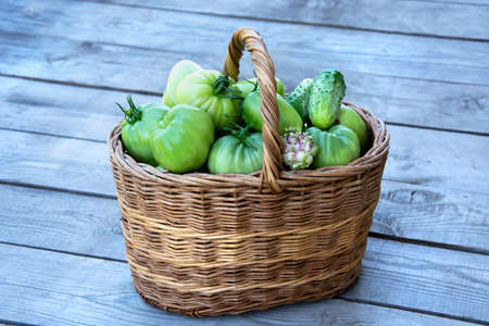 Vegetables in the basket. A wicker basket with tomatoes and cucumbers stands on a wooden background.の写真素材