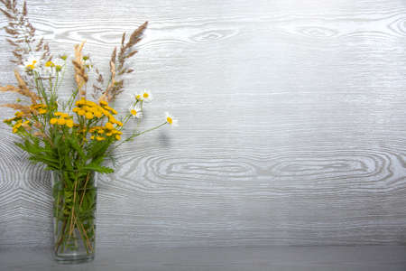 A bouquet of wildflowers in a glass vase on a wooden table with an empty place for text.の写真素材