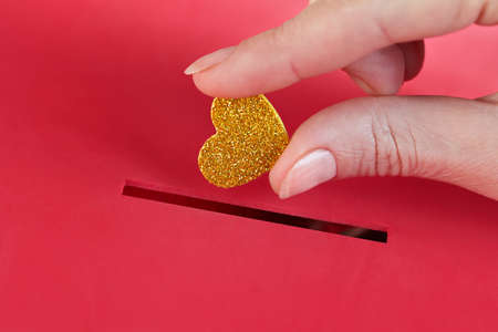 female hand put gold heart into red donation box.の写真素材
