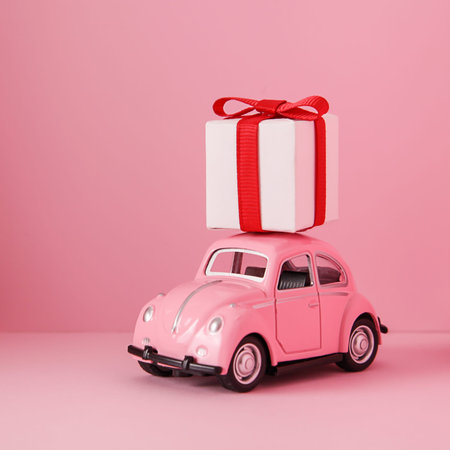 Gift box on toy car on pink background. Christmas holiday celebration concept.の写真素材