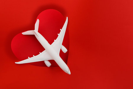 Love of travel. Valentines Day Gifts for Travel Lovers. Travel planning for Valentines day. White plane on red background heart shape. Copy spaceの写真素材