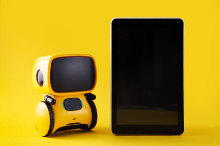 Robot toy and Smart phone on yellow background. Chatbot concept. Tech Gifts for kids. Copy spaceの写真素材