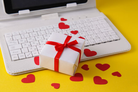 White computer keyboard and gift, heart on yellow background. Shopping online. Valentines gifts. Dating online. Holidays conceptの写真素材