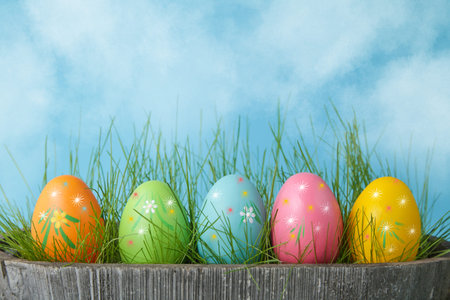 Happy Easter. Colorful Easter eggs in flower pot with grass on blue sky background. Copy space