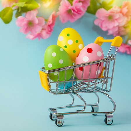 Colorful painted Easter eggs in shopping cart on blue background. Comes out. shoppingの写真素材
