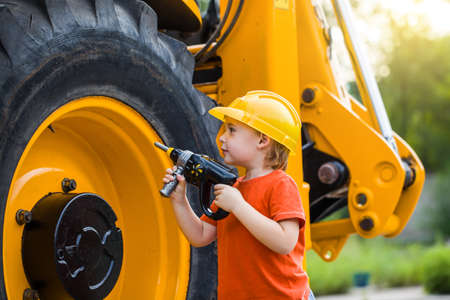 Little boy with toy tools in garage. They are helps father to repair tractor. Involve child in workの写真素材