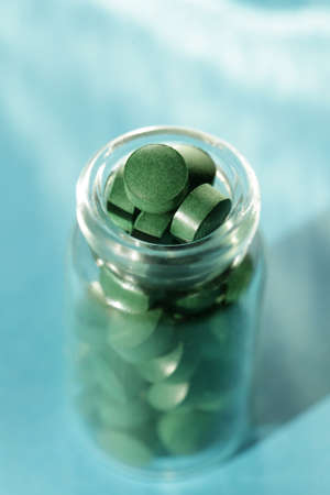 Spirulina pills in glass jars on blue background. Antioxidant nutrition. Bio-energy, biofuel, energy research. Vertical orientationの写真素材