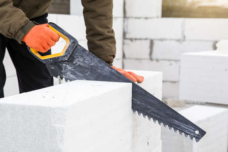 Closeup. Builder sawing aerated concrete block with hand saw at construction site. construction, Building manual workの写真素材