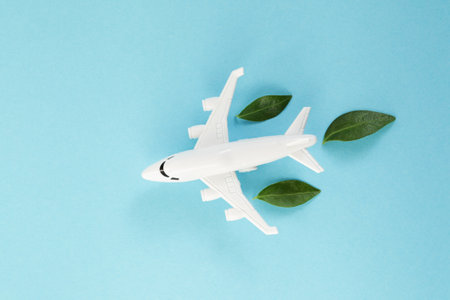 White airplane model emitting fresh green leaves on blue background. Sustainable travel; clean and green energy; and biofuel for aviation industry concept.の写真素材