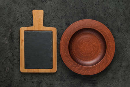 Brown wooden cutting board with slate stone, empty brown clay plate on black stone table. Top view with copy space. Rustic dishesの写真素材