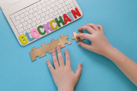 Education. Blockchain for kids. Game Finance. Children hand moves puzzle, laptop on blue background....