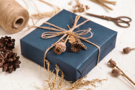 Handmade gift box in dark blue packaging, poppy seed heads, dried flowers on white desk. Gift for man. Floristic, herbarium craft. Natural colours.の写真素材