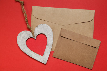 Two Empty brown craft envelope, heart on red background. top view, copy space. Greeting card mockup...
