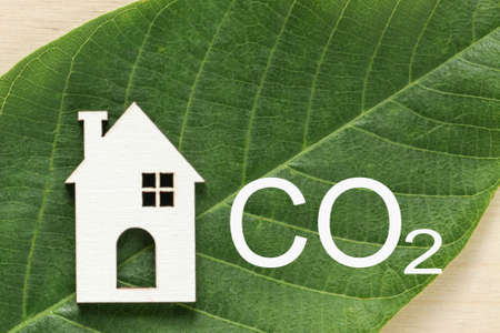 Decarbonization of Real Estate. Lower CO2 emissions and reduce carbon. House, letter CO2 on green leaf background. Sustainable development, environment protectionの写真素材