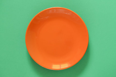 Empty Orange Ceramic Plate on Green background. Top view, copy space. Spring and Summer Menu