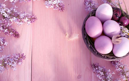 Colorful easter eggs in basket on rustic wooden table.Holiday background with spring lilac flowers. Top view with copy spaceの写真素材