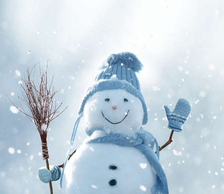 Cute smiling snowman with blue scarf and hat with a broom in his hand.Winter fairytale.Greeting card with copy-spaceの写真素材