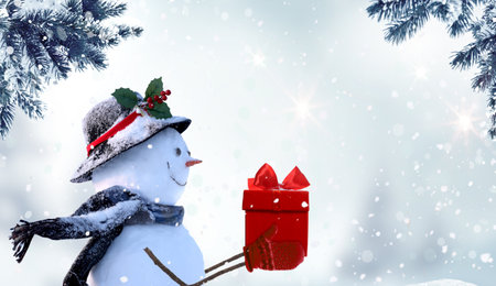 Merry Christmas and happy New Year greeting card with copy-space. Happy snowman with red gift box standing in Christmas landscape. snow background. winter fairy tale.の写真素材