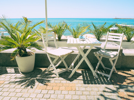 Wooden table and chairs in outdoor cafe at blue sea and palm backgroundの写真素材