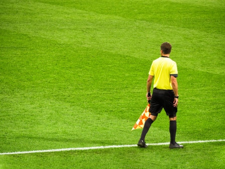 Sochi, Russia - September 30, 2019: Back view of football referee with flag at green grass...