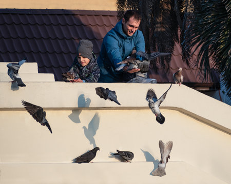 Sochi, Russia - December 8, 2019: Happy father and son feeding pigeons at sunny dayのeditorial素材