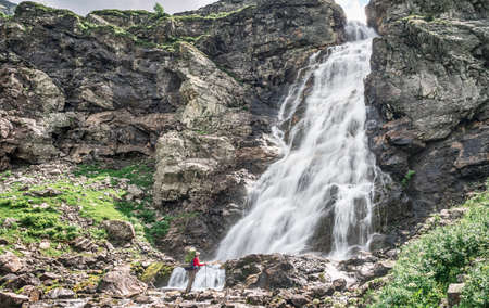 Active man with backpack and tourist equipment looking at big waterfallの写真素材