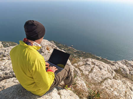 Man working on laptop and sitting on mountain top at sea water backgroundの写真素材