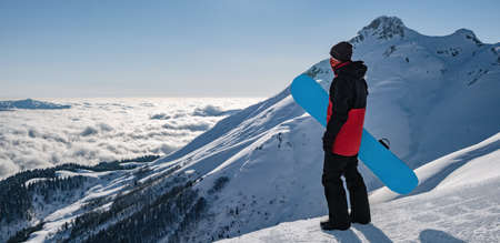 Young active man with snowboard looking at sunset in cloudy mountainsの写真素材