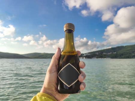 Person holding mini bottle with champagne or sparkling wine at lake backgroundの写真素材