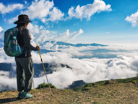 Young active woman with backpack hiking at cloudscape and mountains backgroundの写真素材