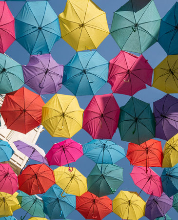 Many colorful open umbrellas hanging above street in daylight at blue sky background. Bottom view. Not AIの写真素材