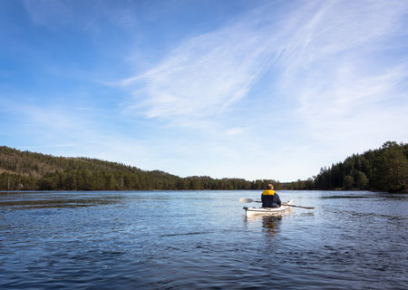 Adult man paddling Norwegian river in white kayak in Nidelva, Norway