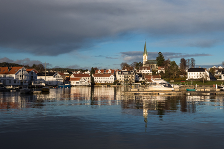 Lillesand, Norway - November 10, 2017: Lillesand City seen from the harbor. Blue sky and clouds, reflections of city in the ocean.のeditorial素材