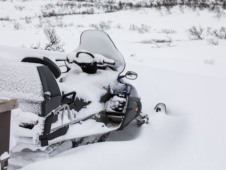 A snow mobile parked outside is covered in snowの写真素材