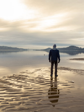 Man standing at the beach, reflections of the man in the water. Calm sea, mist and fog. Hamresanden,...