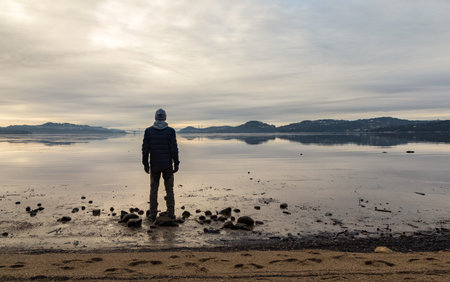 Man standing at the beach, looking at the calm sea and the mist and fog. Hamresanden, Kristiansand, Norwayの写真素材