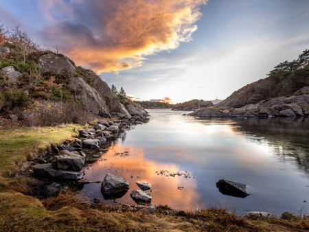 Evening light, ocean, stones and rocks by the seaside, warm light and sunset in the background.