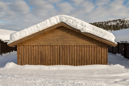 Snow on the roof of a brown building, white clouds on blue skyの写真素材