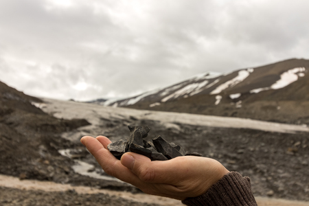 Female hand holding coal found by the Longyear glacier, wich is seen in the background. Arctic landscape of glacial moraine stones and mountains, Longyear valley, Svalbard.の写真素材
