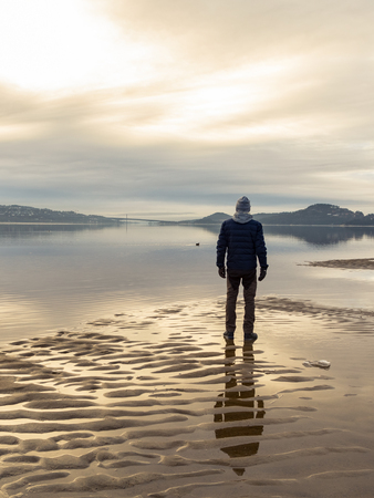 Man standing at the beach, reflections of the man in the water. Calm sea, mist and fog. Hamresanden, Kristiansand, Norwayの写真素材