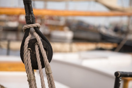 Pulley for sails and ropes made from wood on an old sail boat, with sail and other boats out of focus in the background.の写真素材