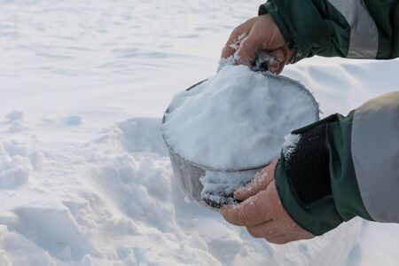 Man holding a pot full of snow, for melting into drinking water. Snow in the background.の写真素材