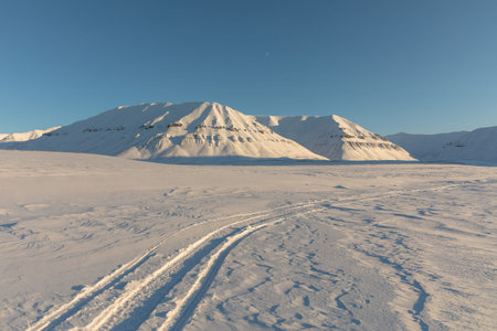 Snowmobile tracks in arctic winter landscape with snow covered mountains on Svalbard, Norway