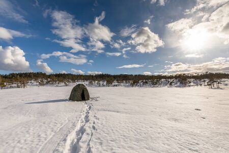 Camouflage tent on a snow covered bog with cloudy sky above. This marsh is an area for the black grouse lekの写真素材
