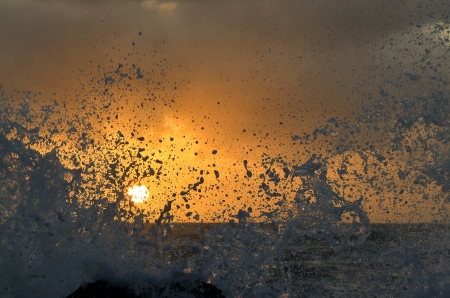 Splashes of high waves obscure the sunの写真素材