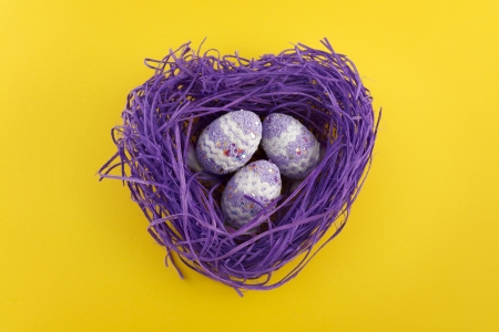 Heart shaped violet nest with Easter decorated eggs on yellow backgroundの写真素材