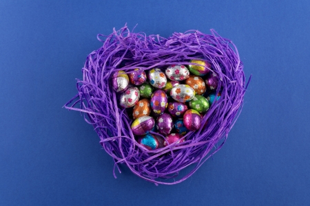 Heart shaped nest with chocolate Easter eggs on blue backgroundの写真素材