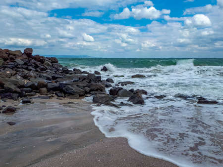 Black sand beach with rocks and waves at the Black Sea coast in Pomorie, Burgas Bay, Bulgaria in summer.の写真素材